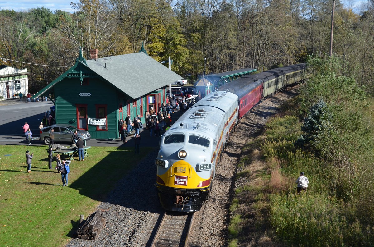 Aerial view of train station with a crowd of approximately 40 people outside waiting for the approac