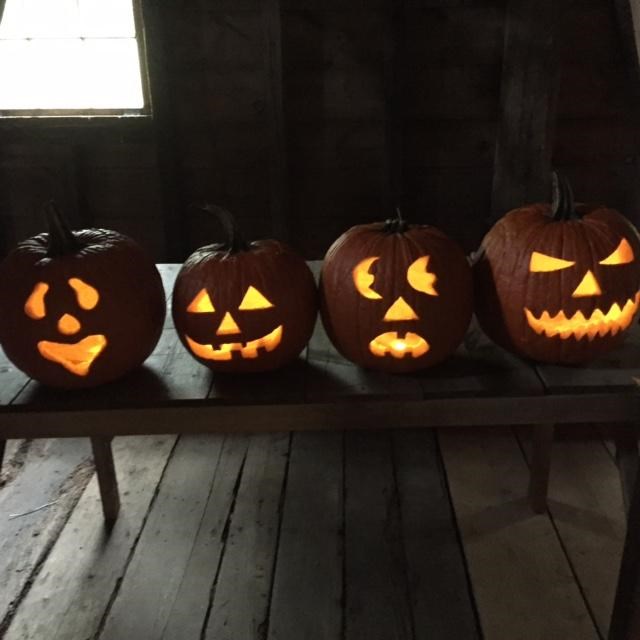 Four lit jack o lanterns on a wooden bench