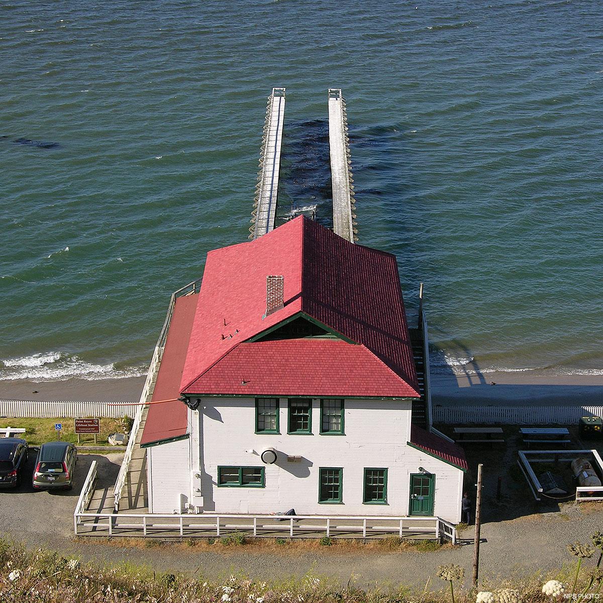 A red-roofed, white-sided building at the water's edge with a dock extending into the water.