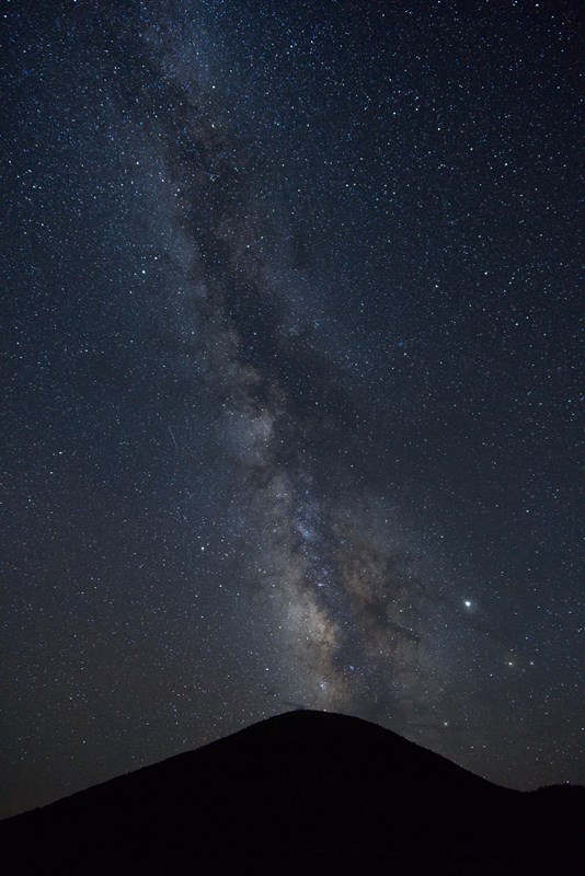 Milky Way and stars in the night sky appearing to erupt from the silhouette of Capulin Volcano