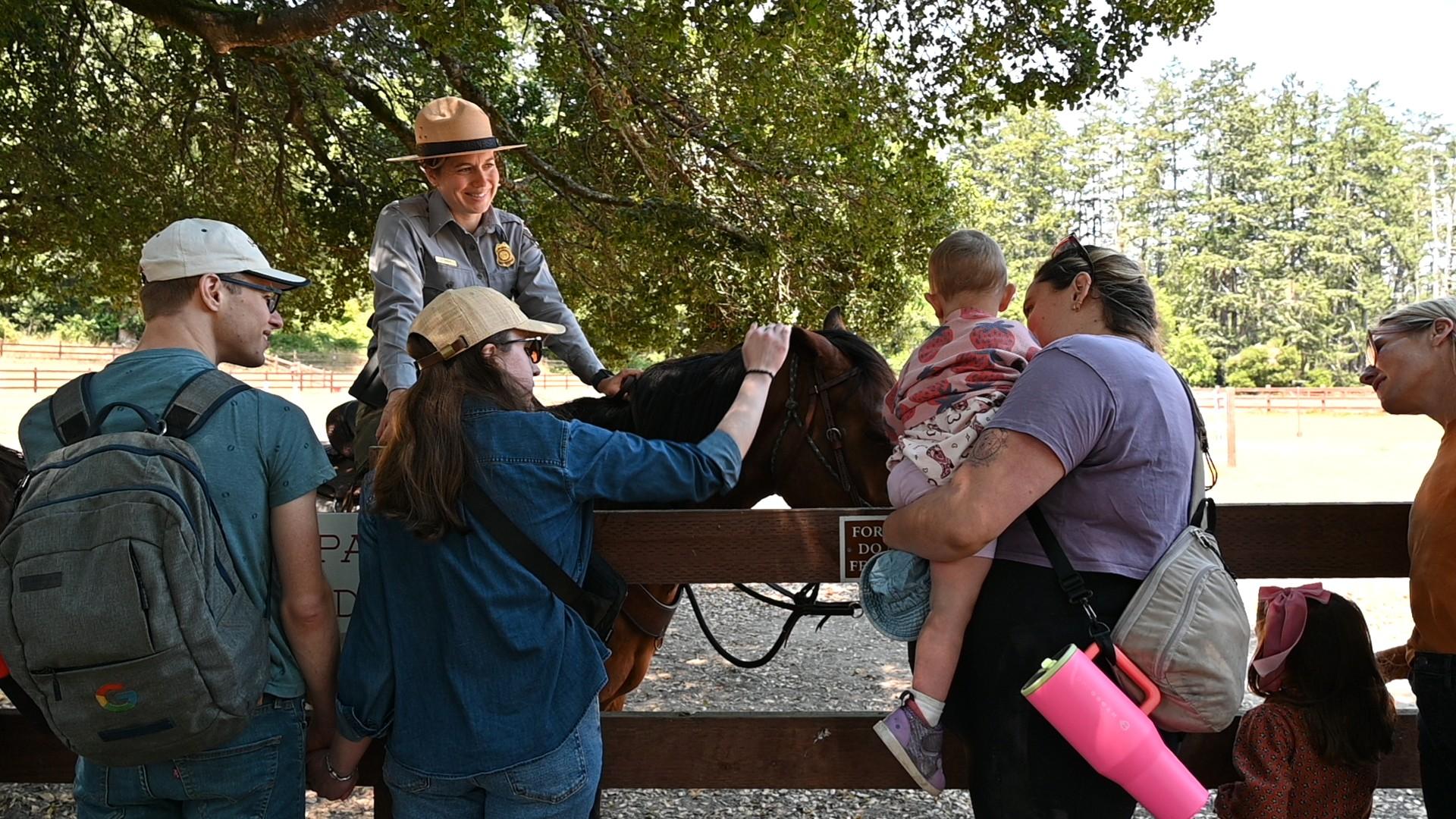A ranger on horseback greets a family over a wooden fence.