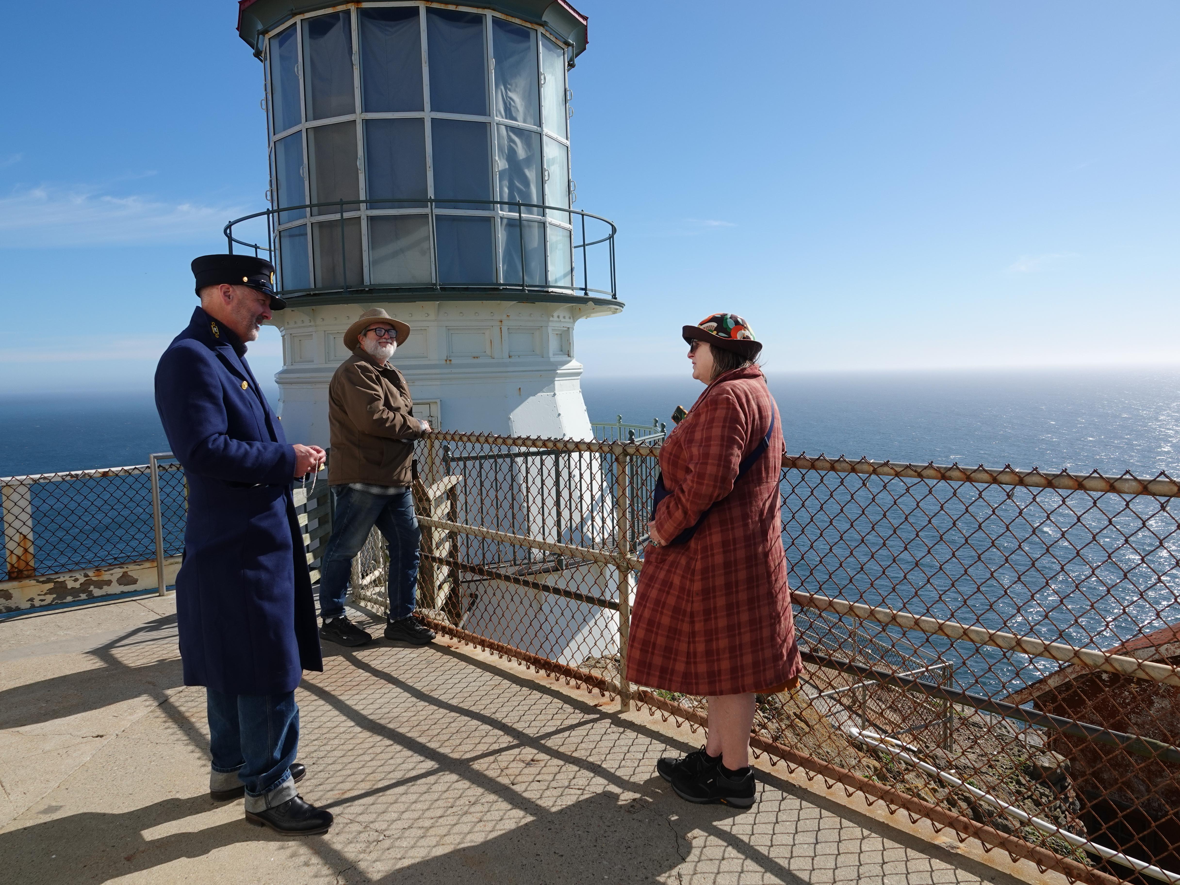 A ranger dressed as a historic lighthouse keeper speaks to two people outside a white lighthouse.