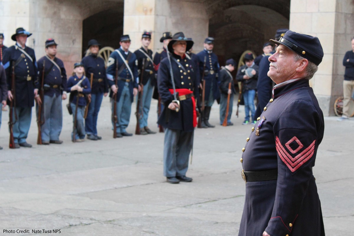 Man in Civil War uniform in right foreground facing left with other uniformed men in background