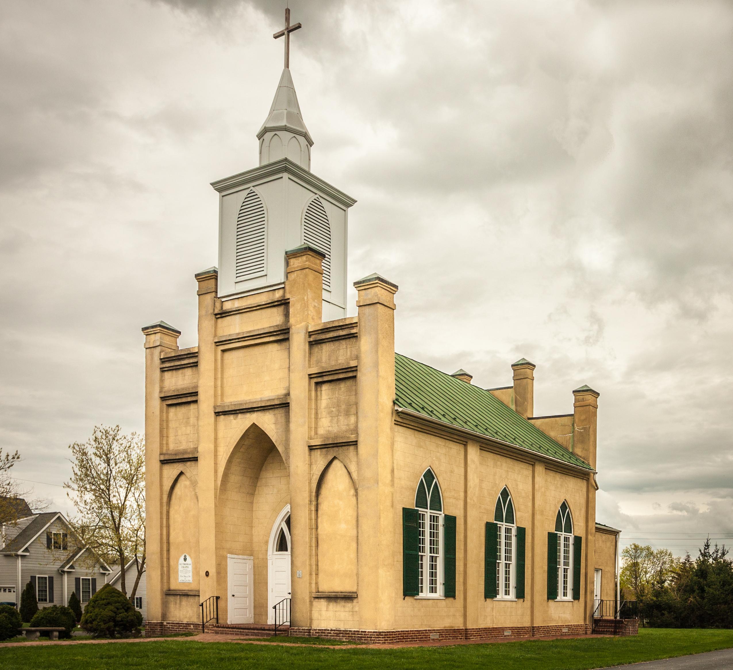 A buff-colored Gothic Revival church stands on a small town street.
