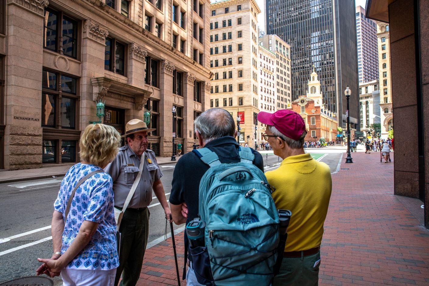 A ranger stands in front of the old state house with a crowd of visitors around him