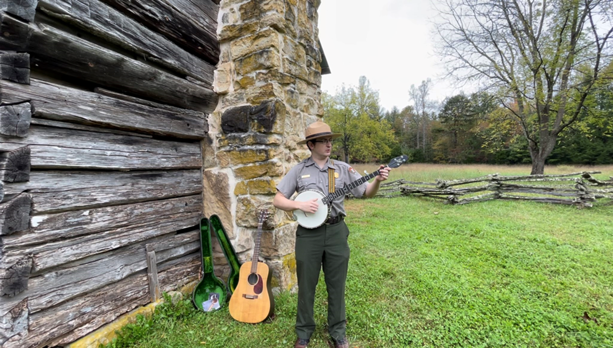 Ranger playing a banjo in front of historic cabin