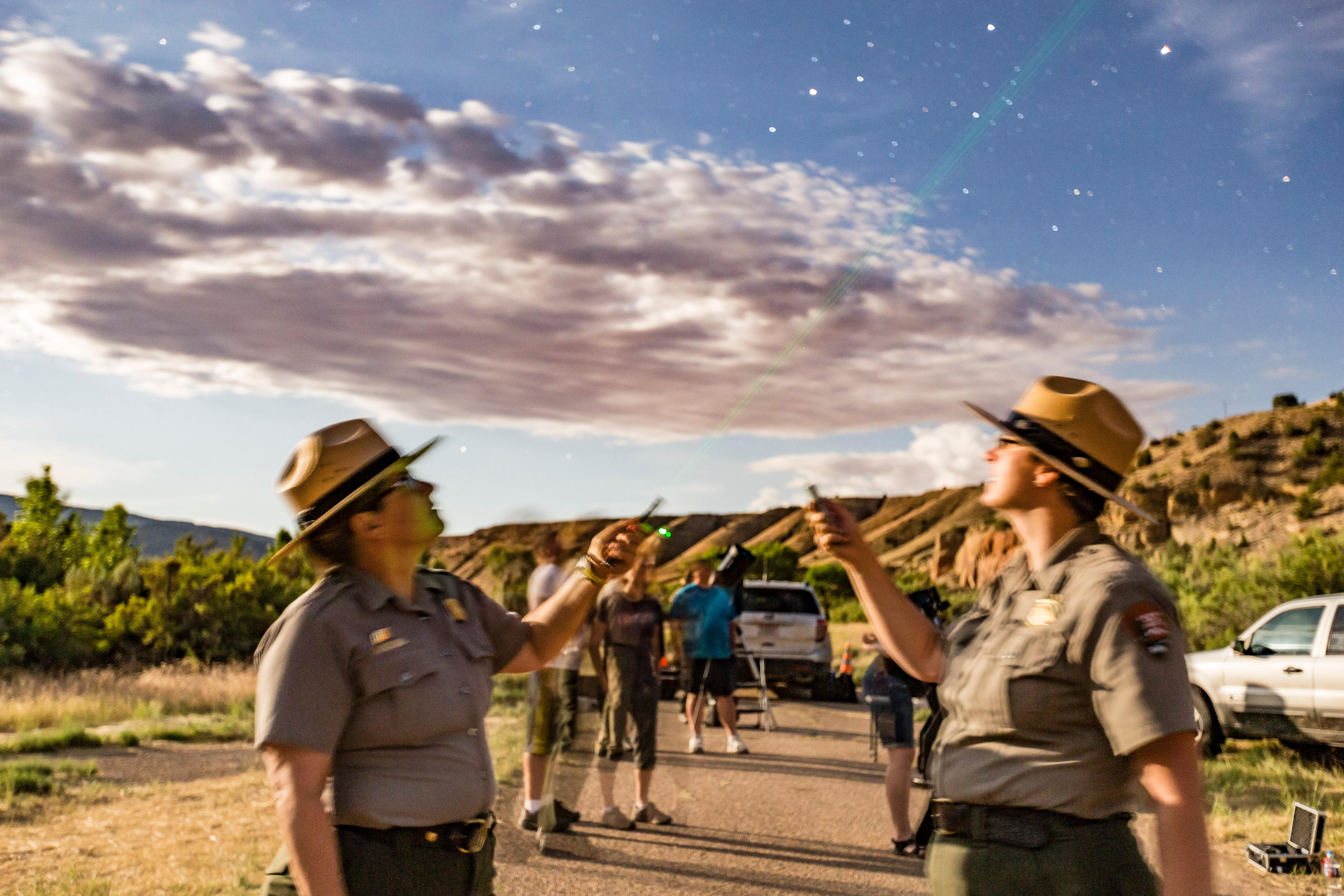 Two rangers use green laser pointers to point out stars to a group of visitors.