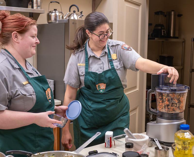 Two rangers in green aprons work in a kitchen.