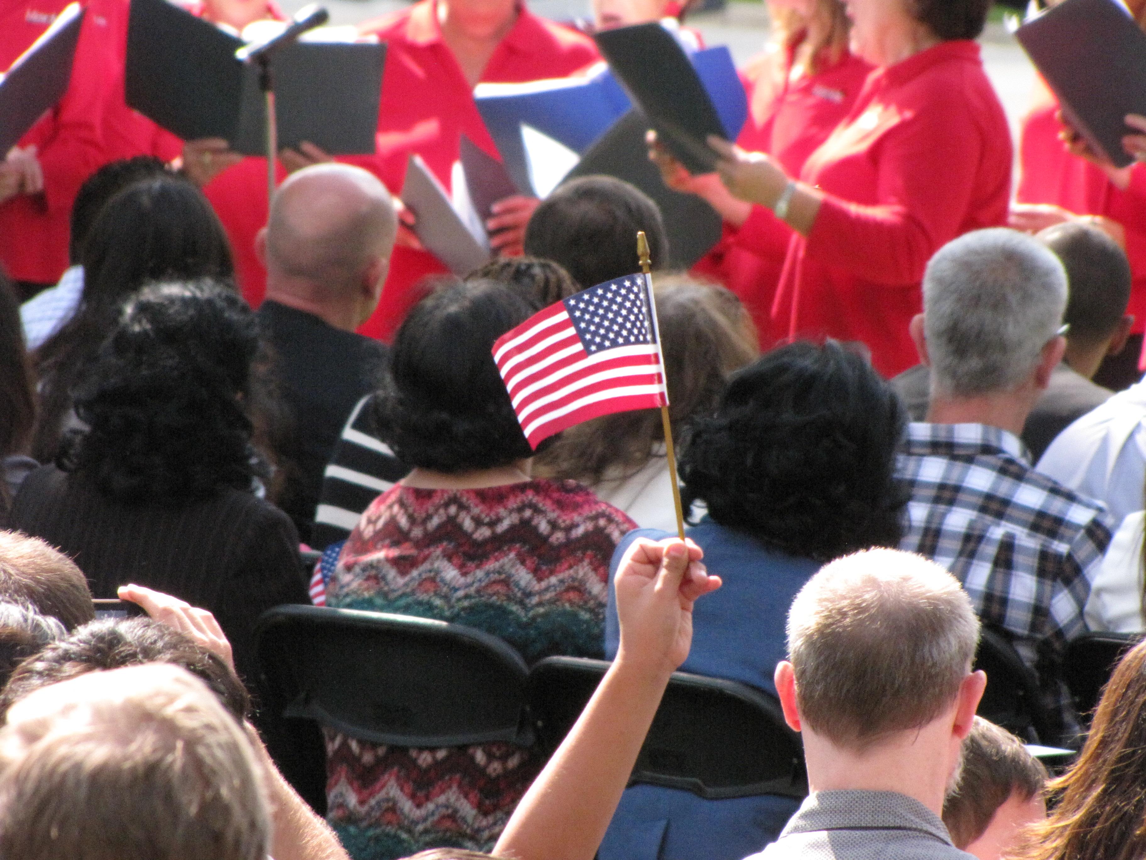 A person in a crowd holds up a small American flag.