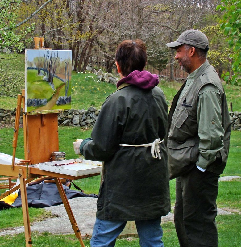 A painter paints with an easel on a gloomy day with a man standing next to her giving advice.