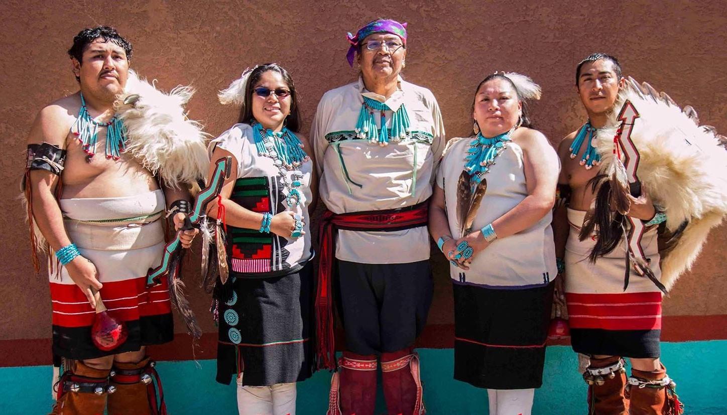 5 Zuni dancers, wearing ceremonial clothes are posing for a group photo.