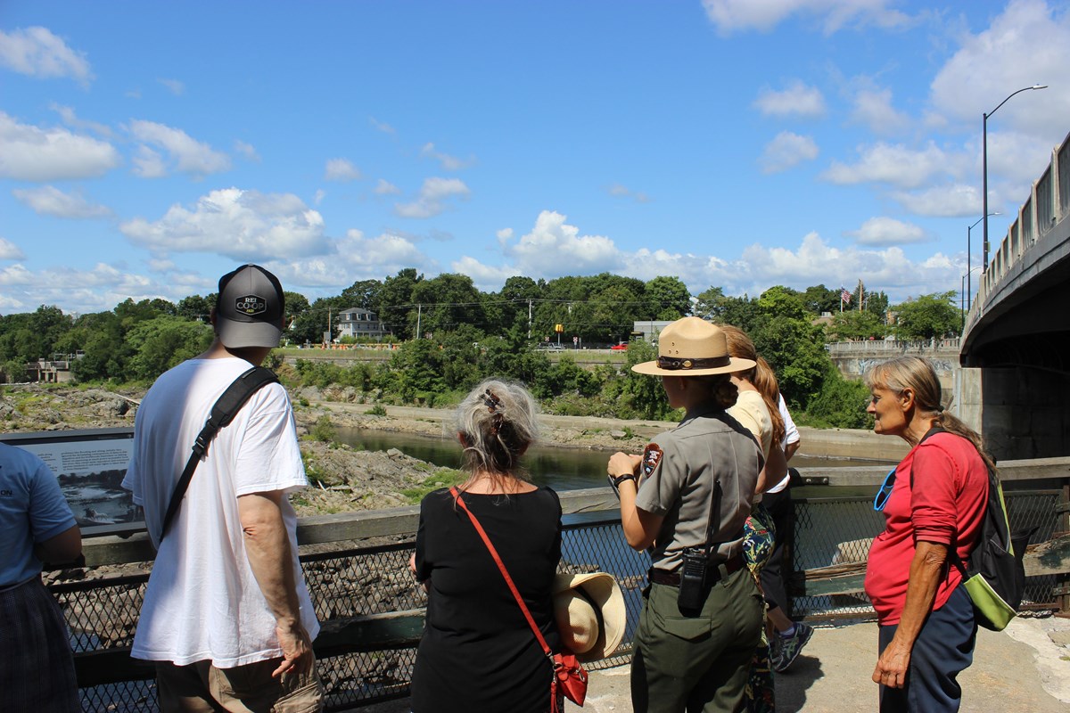 A uniformed park ranger speaks to a group of visitors along one of Lowell's waterways.