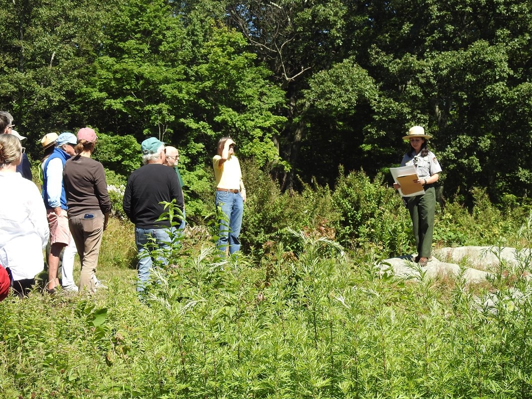 A ranger leading a group, holding up an image, in front of a pond.