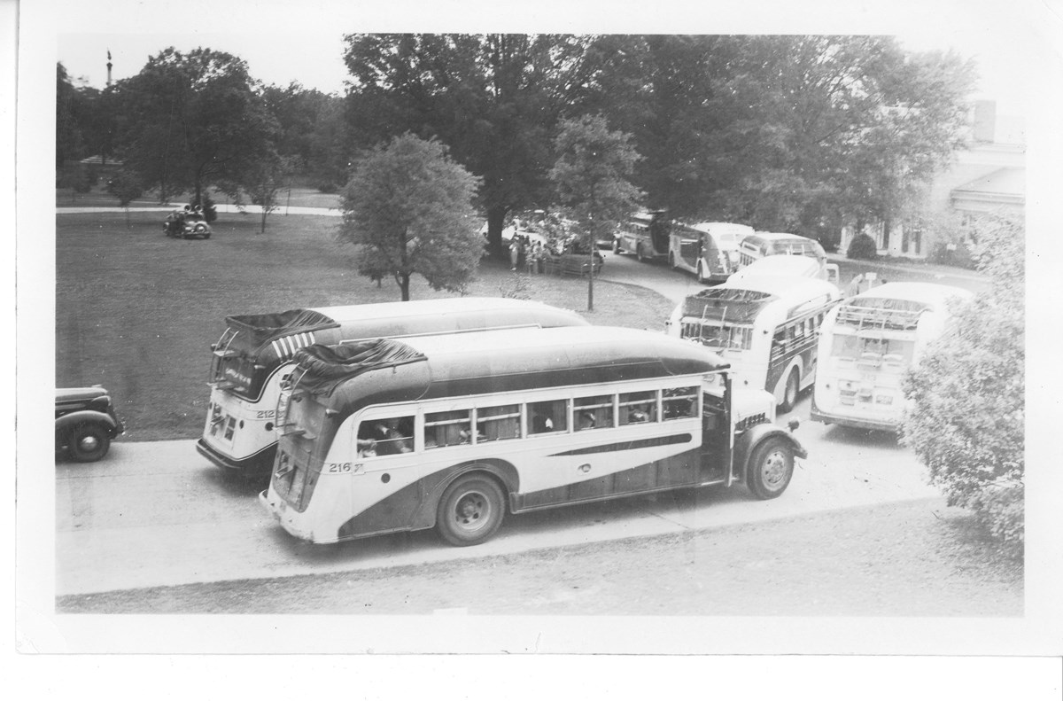 Black and white image of 1930s era busses in front of visitor center.