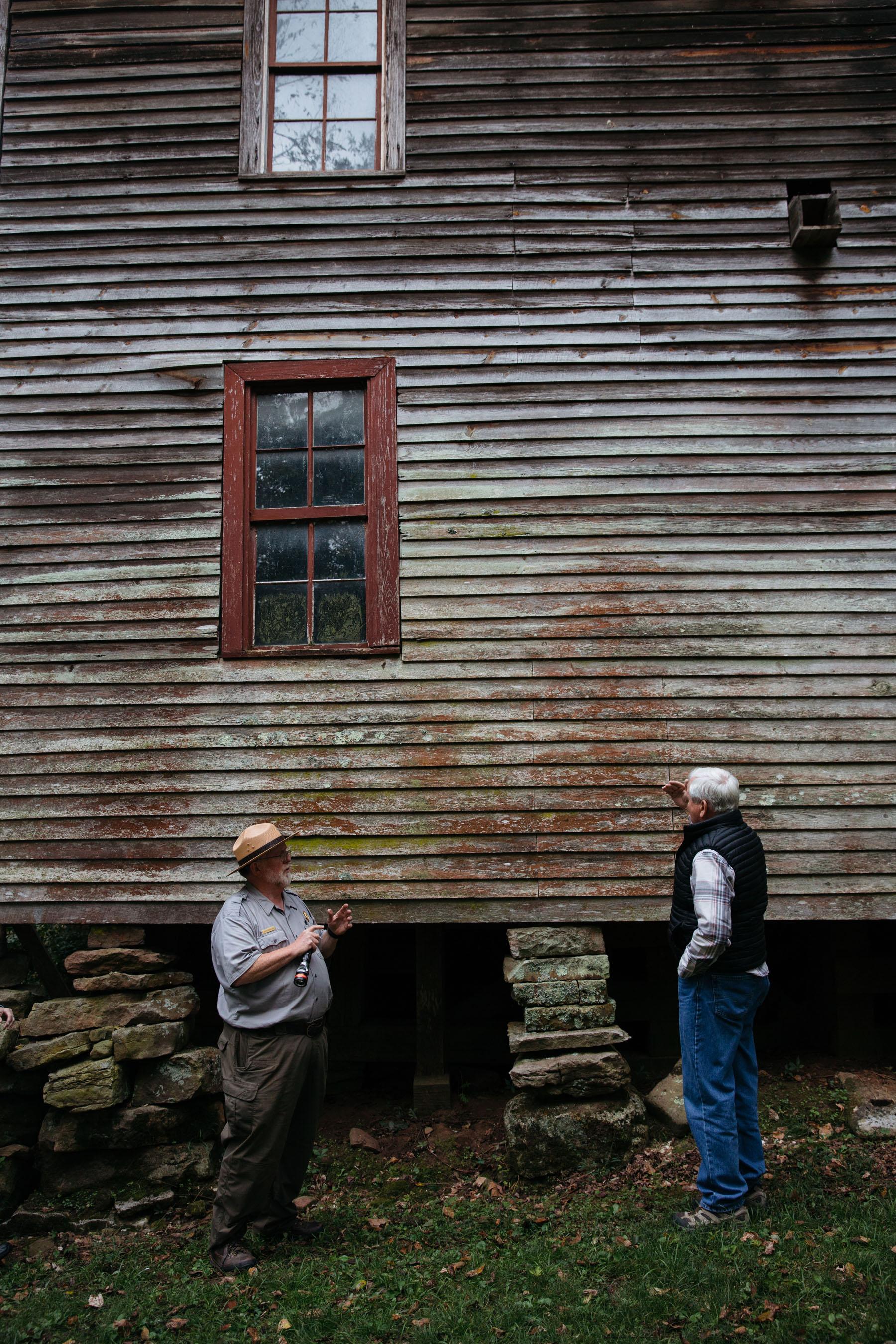 A ranger stands in front of a wooden mill.