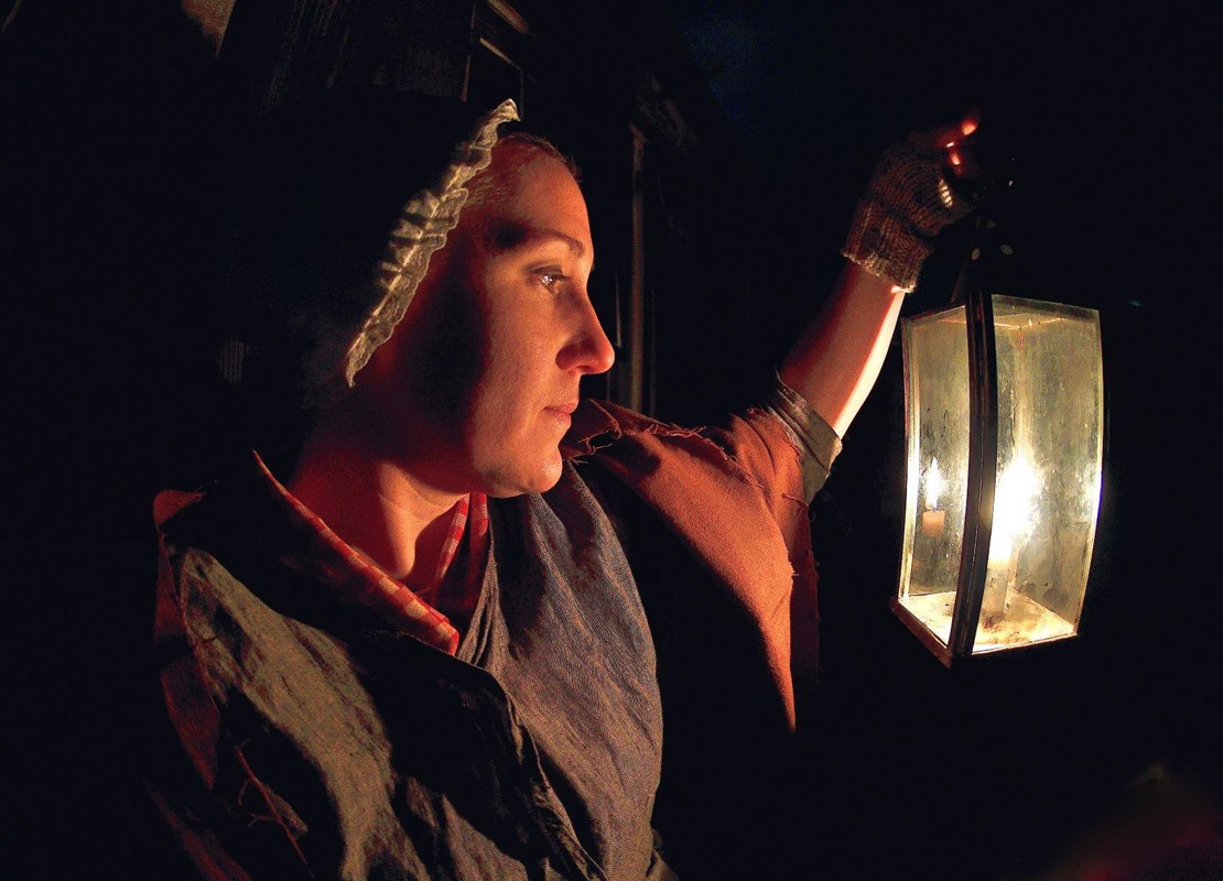 A woman stands in a darkened room, her face illuminated by soft candlelight.