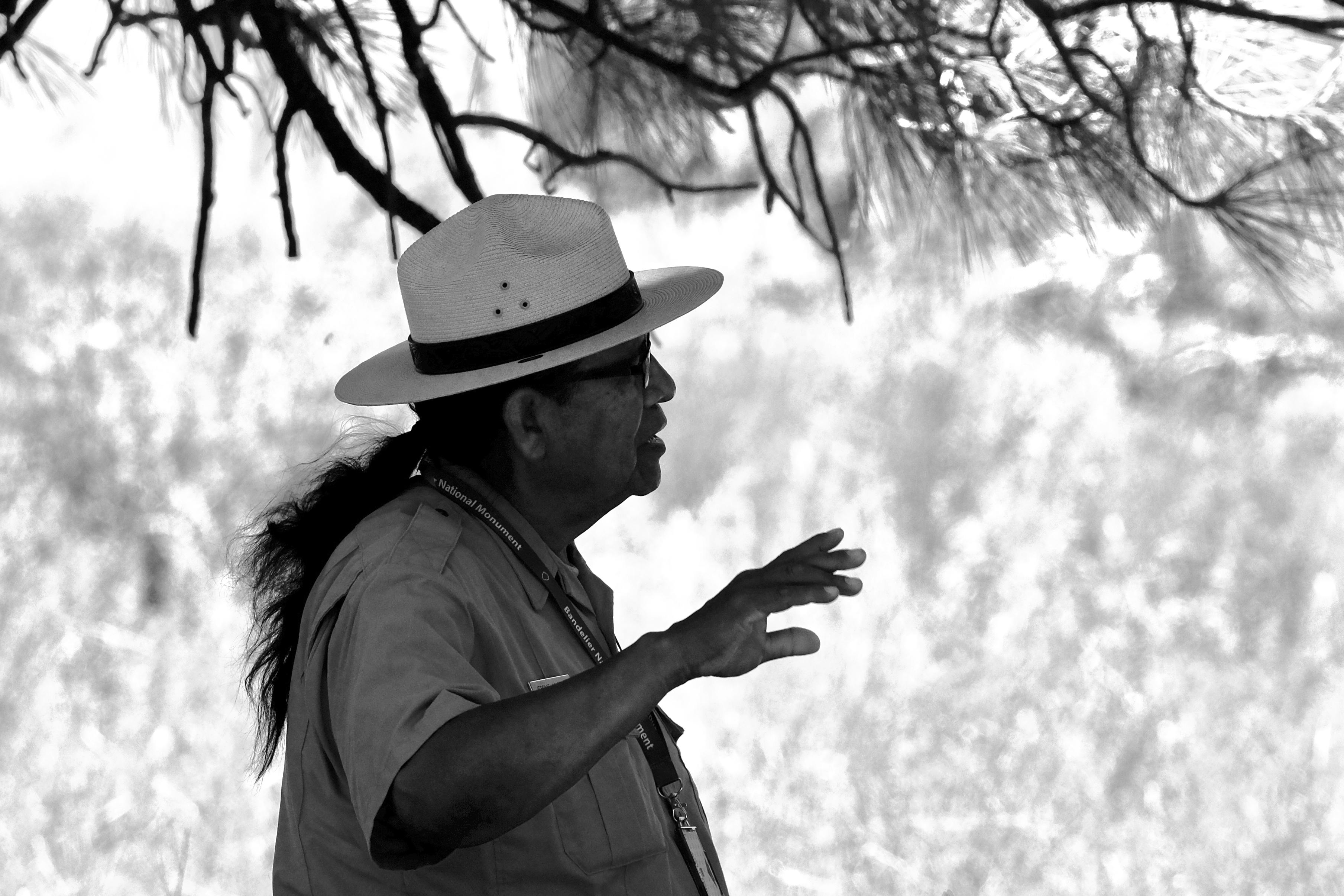 A black and white scene of a ranger talking underneath a ponderosa pine tree.