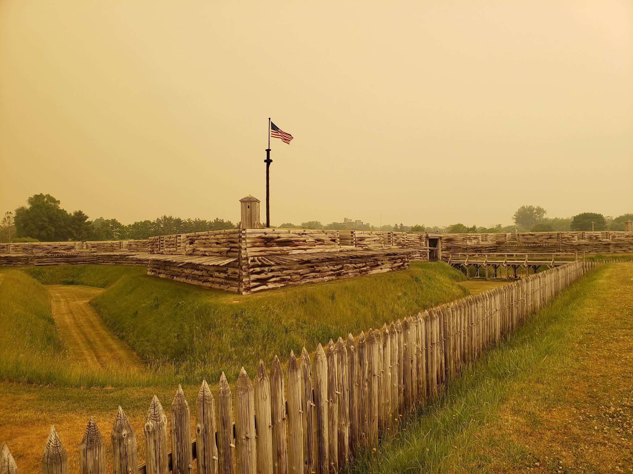 An eerie yellow, hazy sky surrounds the wooden fort. It makes it look strange.