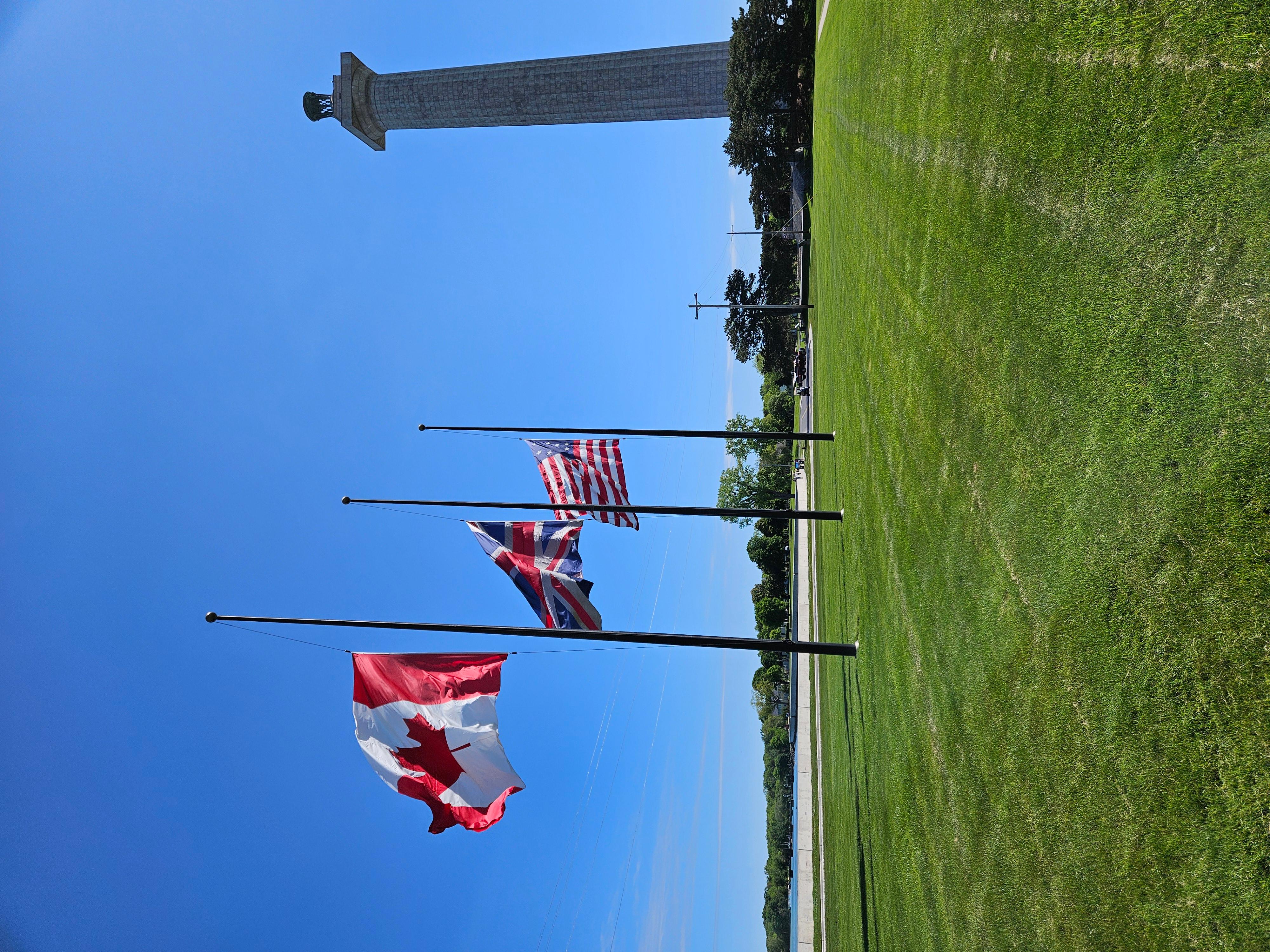 Three flags at half-staff with a tall stone monument in the background