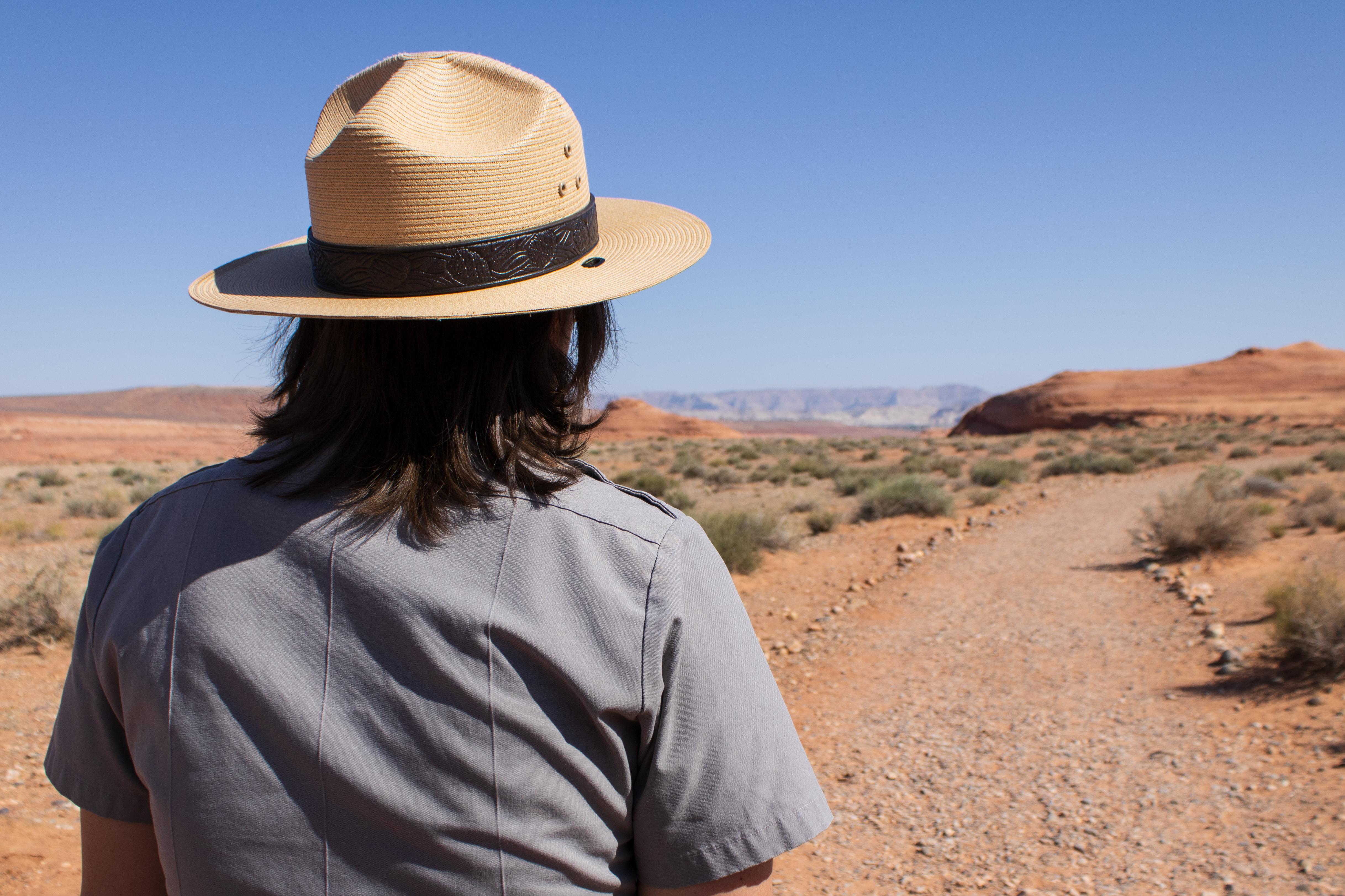 A Park Ranger walks down a sandy desert trail.