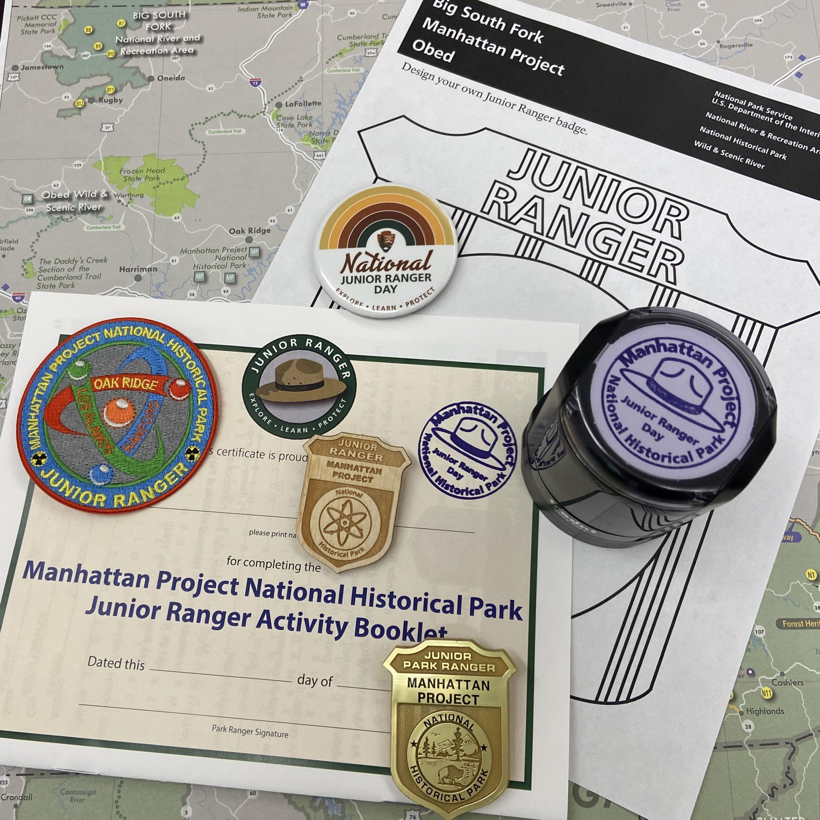 A junior ranger book, badges, patch, pin, and stamp are on top of a worksheet and map of East Tennes