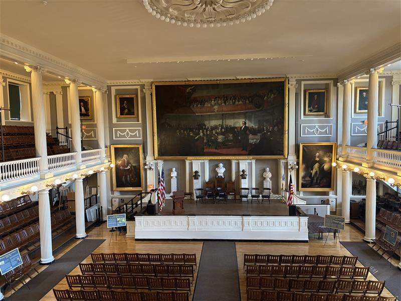 Photo of a big hall with a balcony, stairs on the floor, and artwork adorning the walls