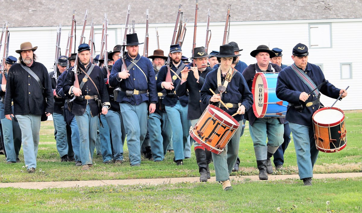 Men in blue uniforms marching. Two are playing drums.