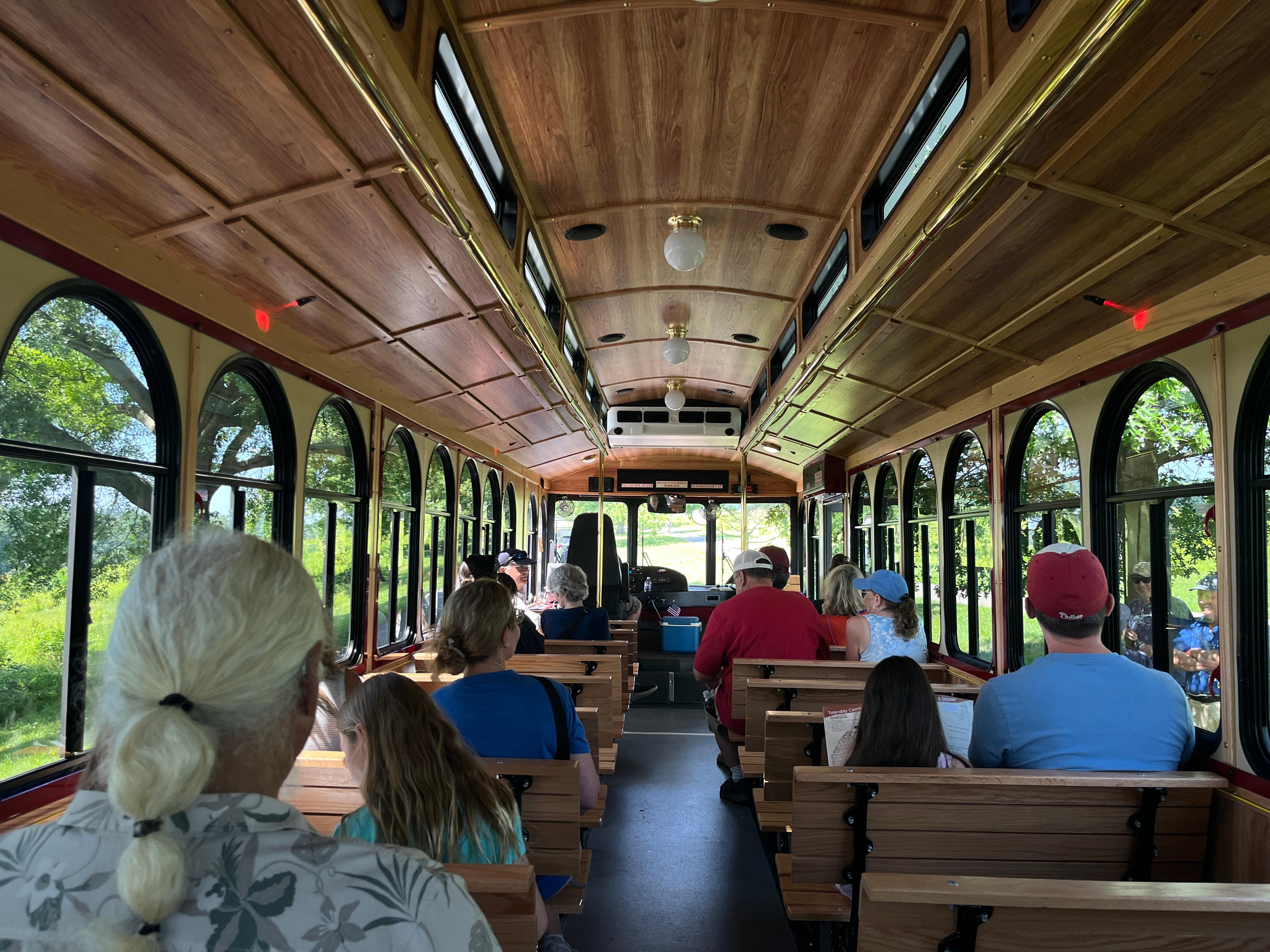 wood paneled interior of a large trolley with large windows people sitting in seats facing the front