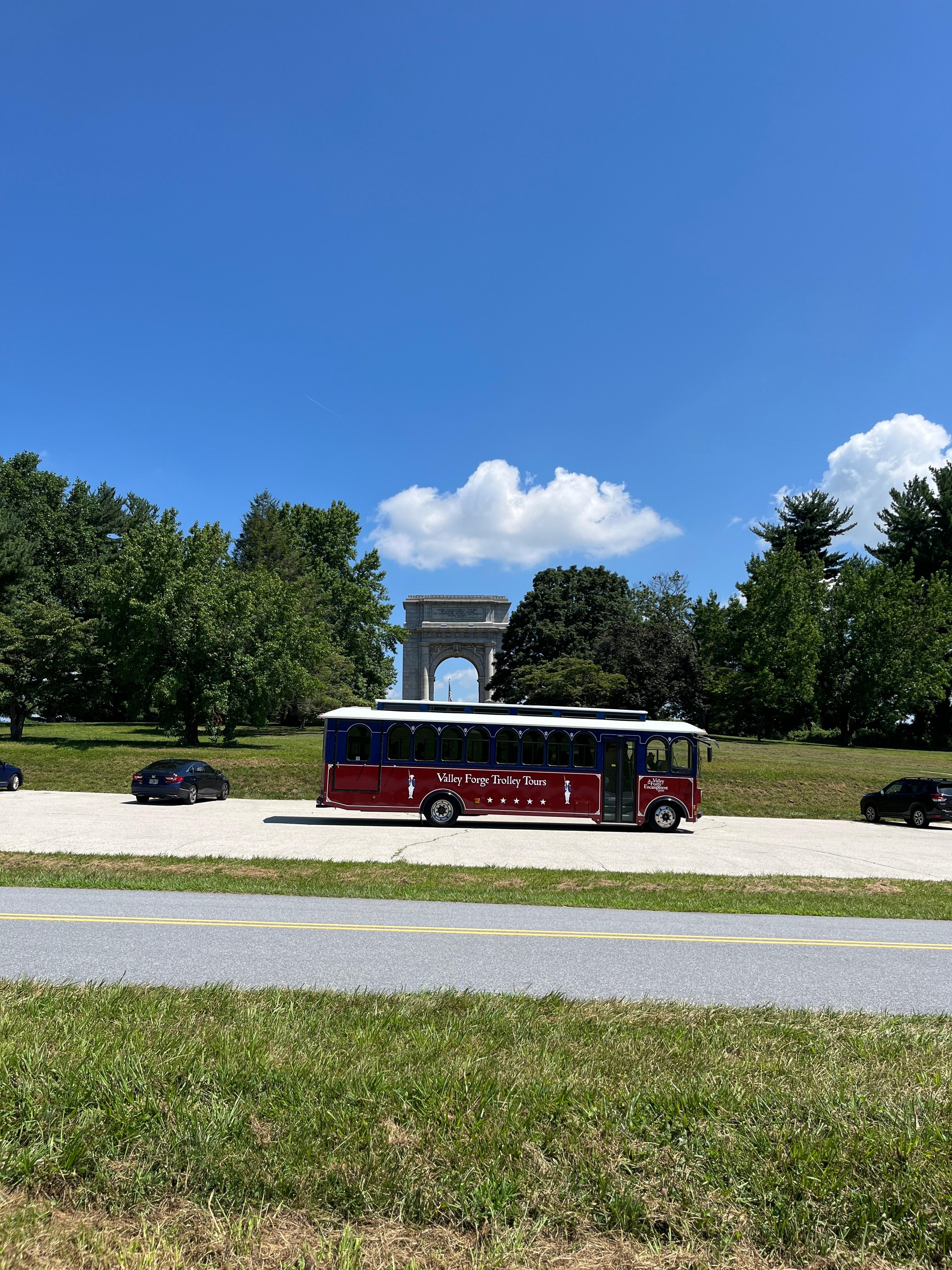 A red trolley the size of a bus in front of the National Memorial Arch monument at Valley Forge