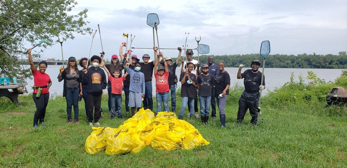 A group of triumphant kids and adults stand behind a mound of full trash bags