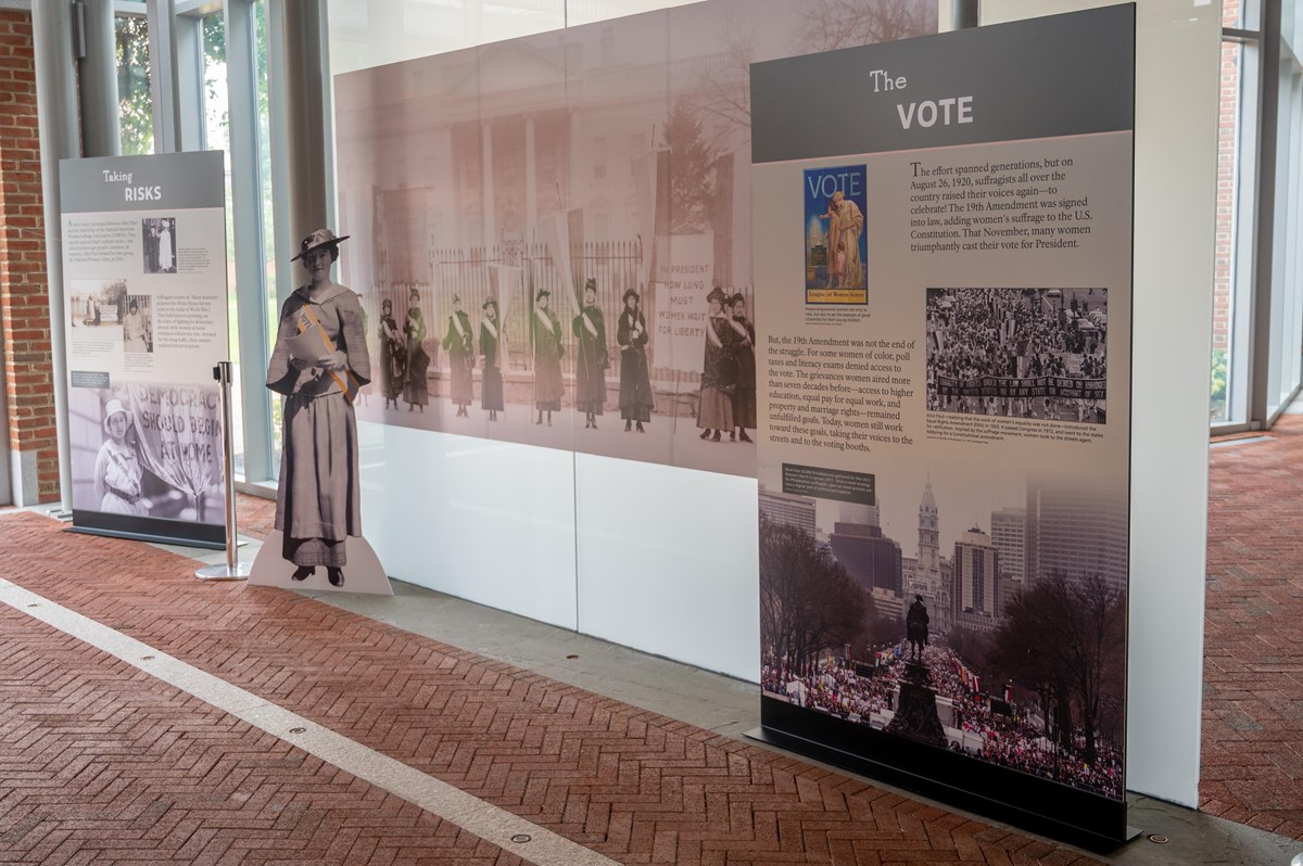 Exhibit panels featuring images and text about women's voting rights flank a cardboard suffragist.