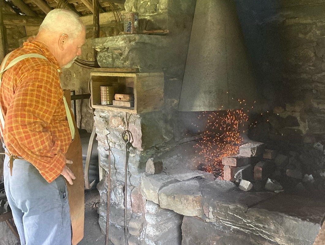Historic demonstrator in living history apparel tends a fire in the blacksmith shop.