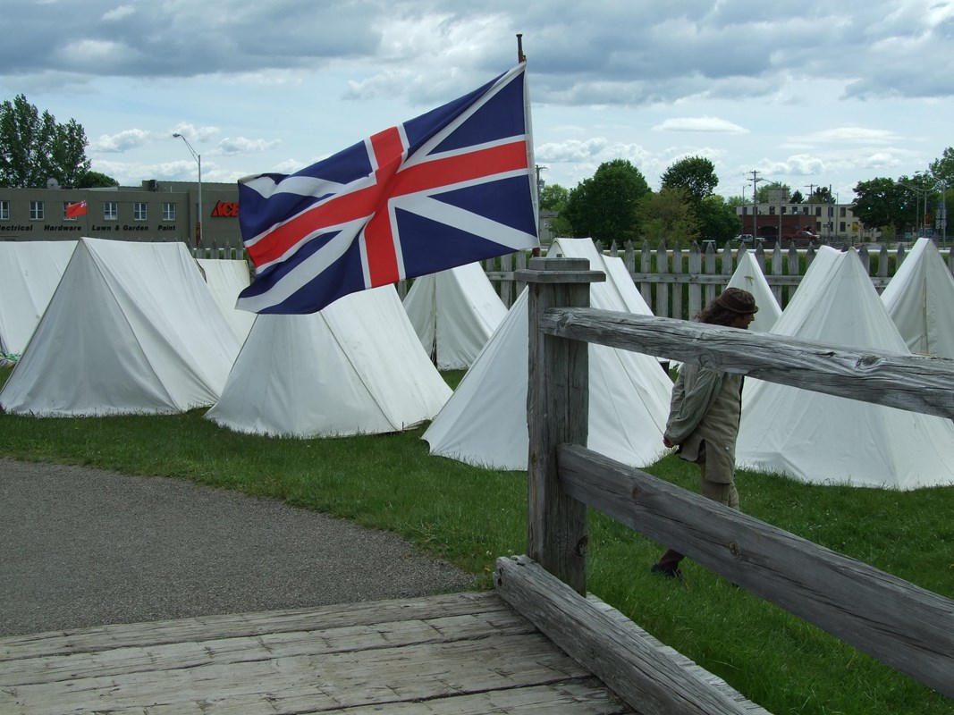 A British-style flag blows in the wind near a bunch of large, white canvas tents.