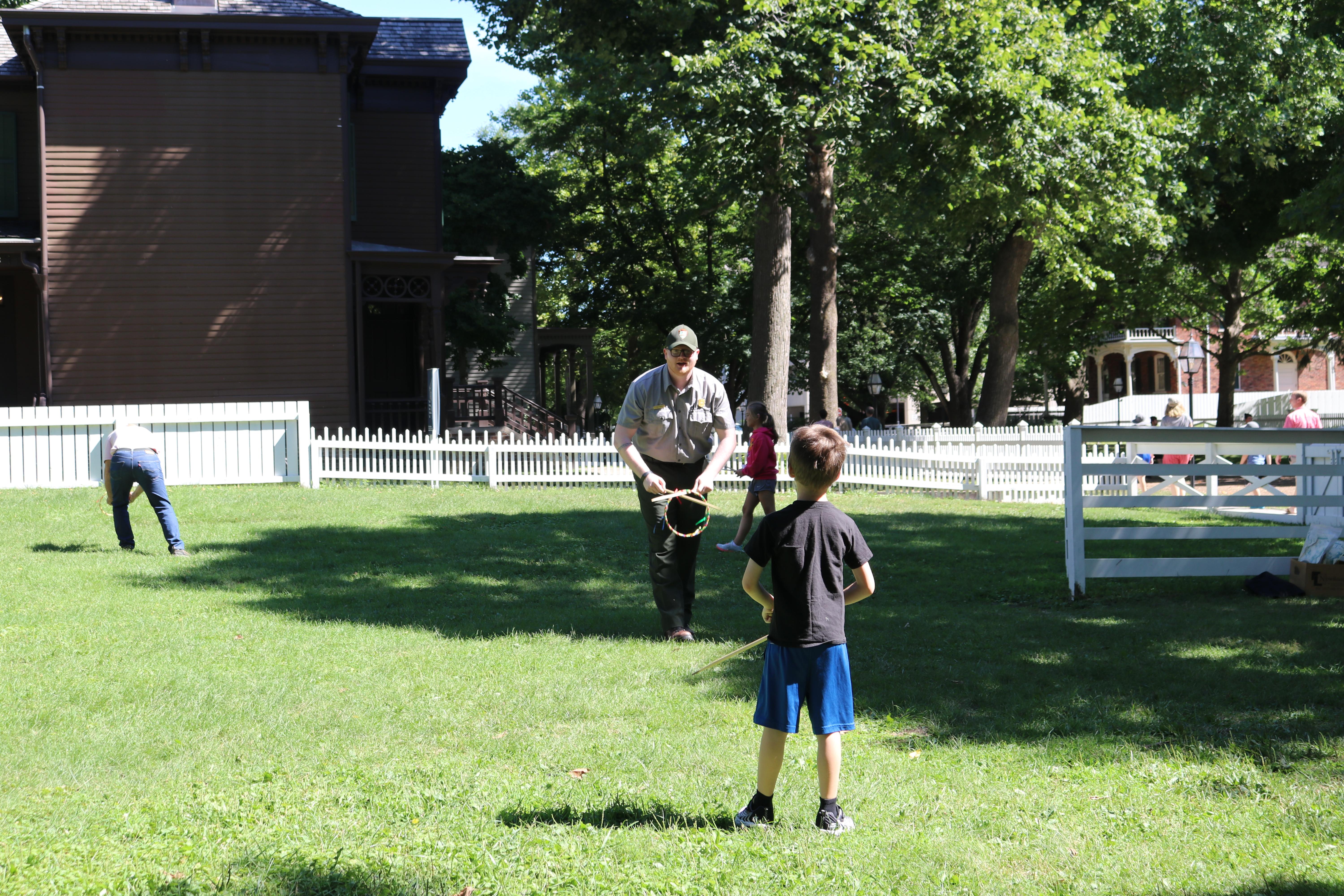 A ranger and a child play a game of graces in a grassy lot.