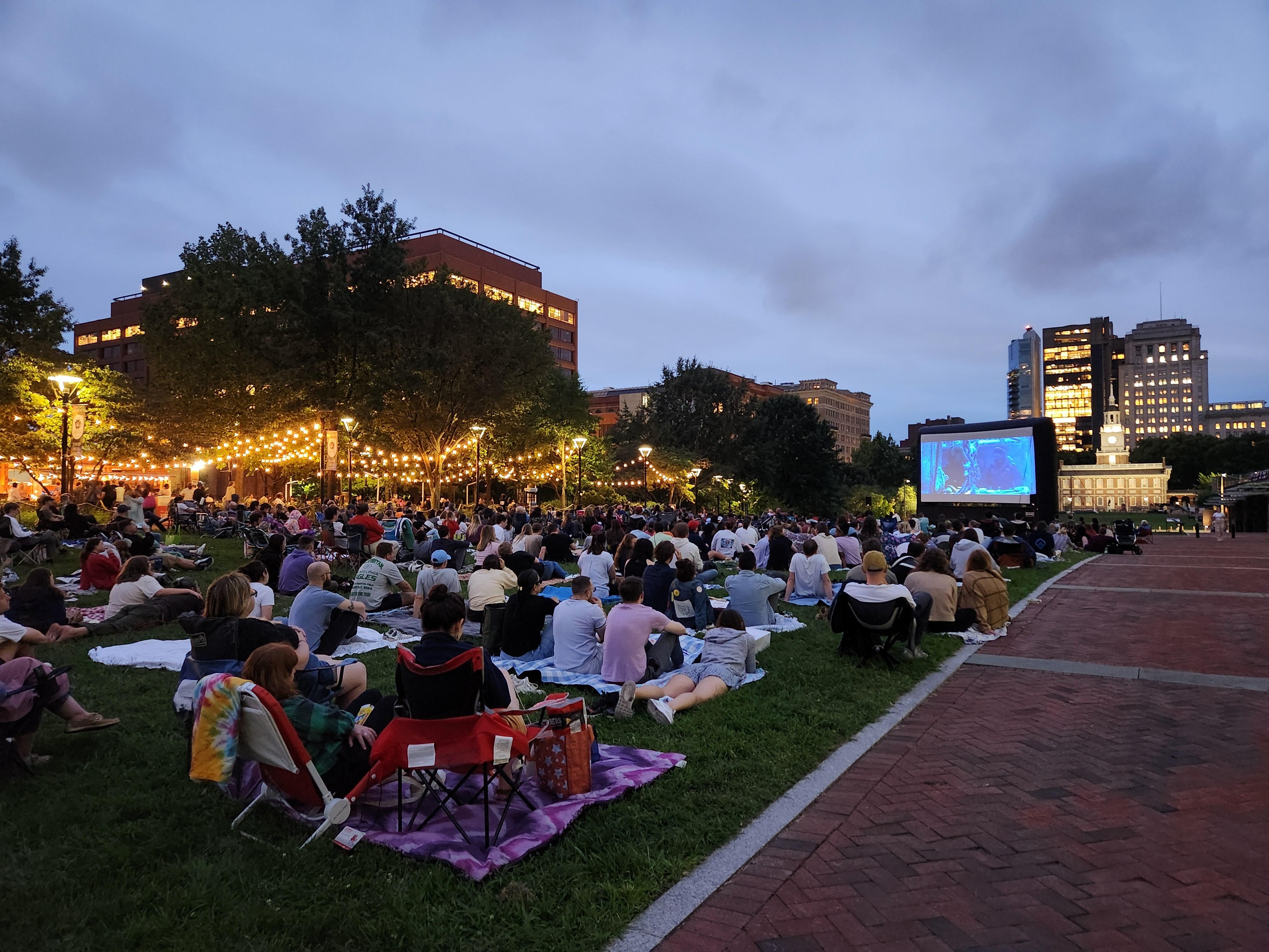 A crowd gathered on a grassy mall watching a movie.