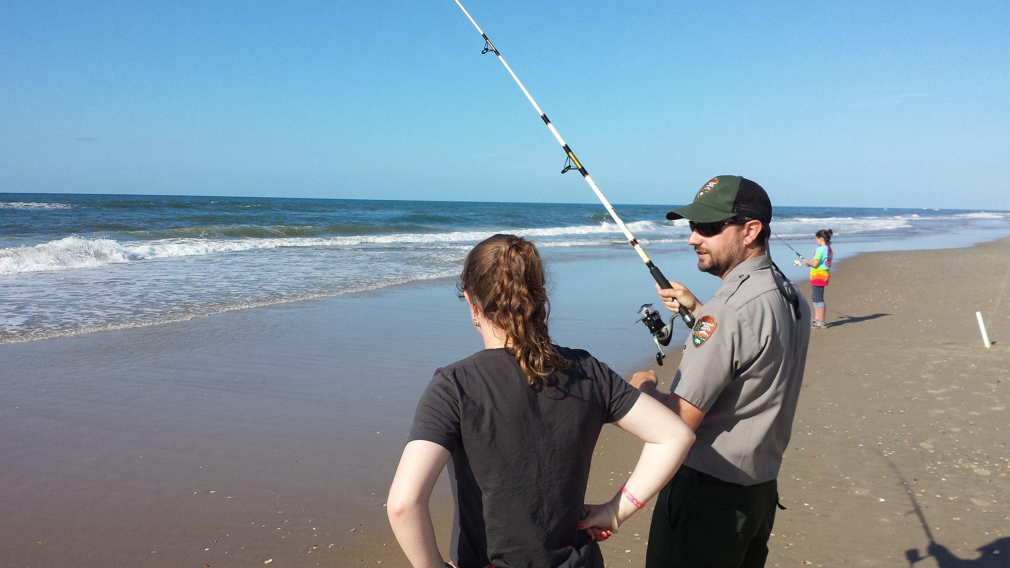 A ranger fishes with a visitor on the beach.