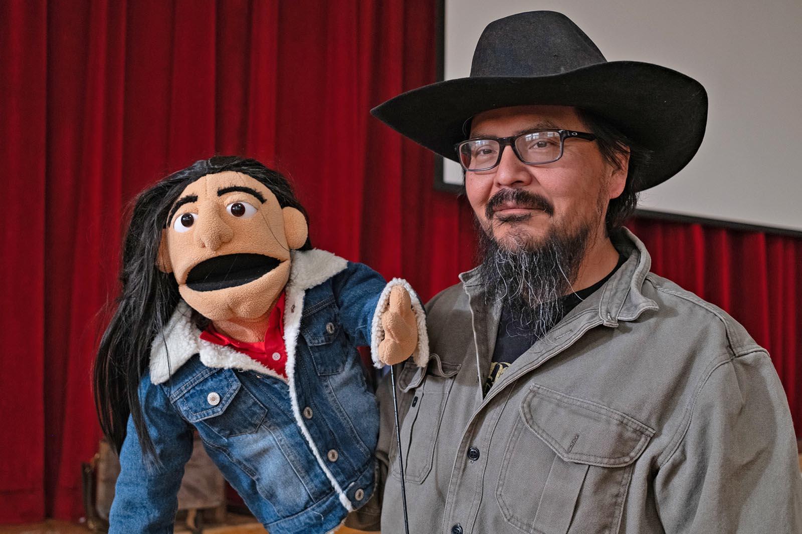 Holding a large puppet, a middle-aged man with a long black beard and hat
