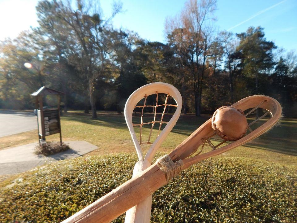 Two wooden stickball sticks crossed with a small leather ball in the stick net.