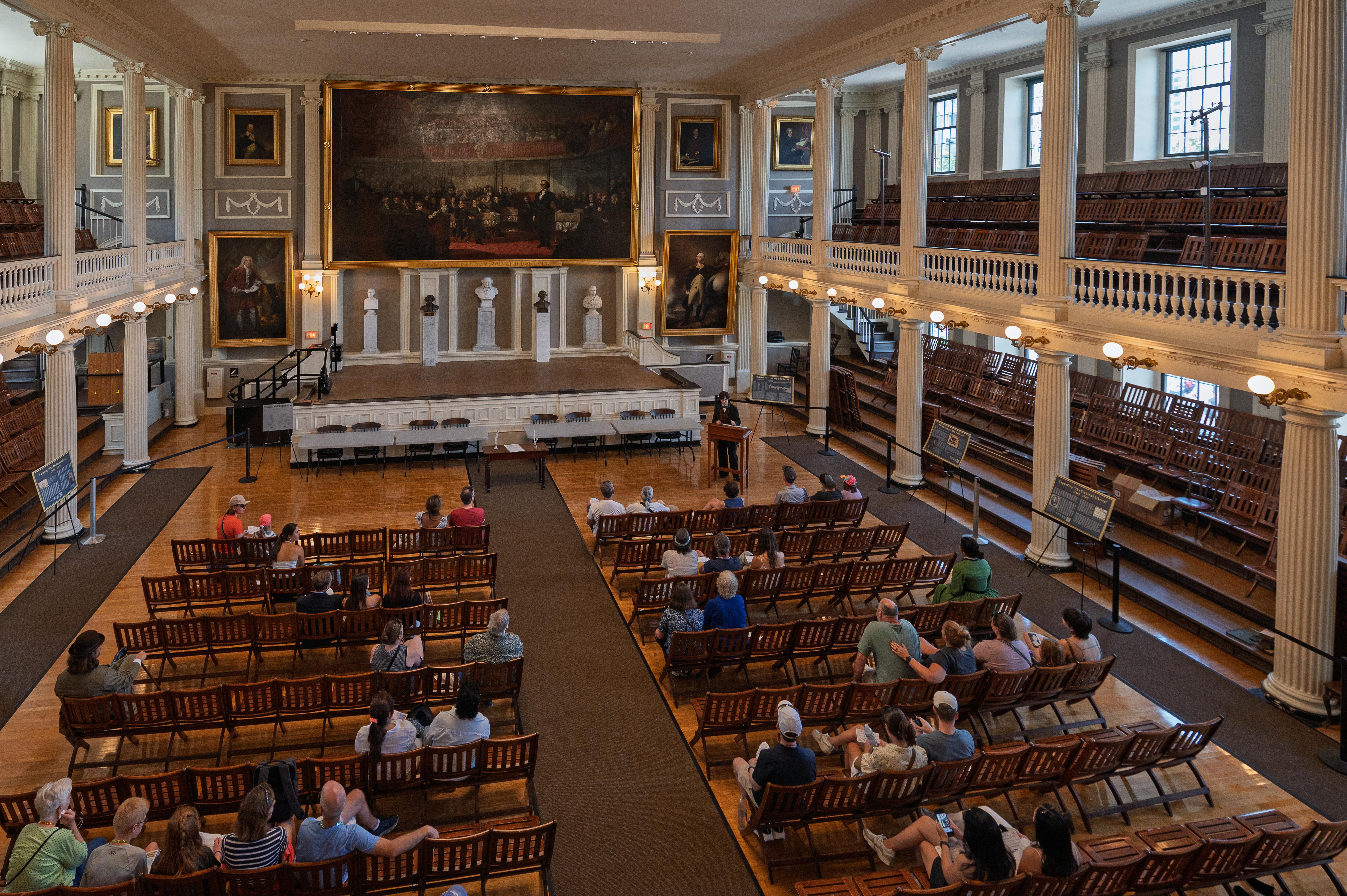Image of the Great Hall from above. A crowd sites in the chairs a Ranger is in front in 1800 cloths