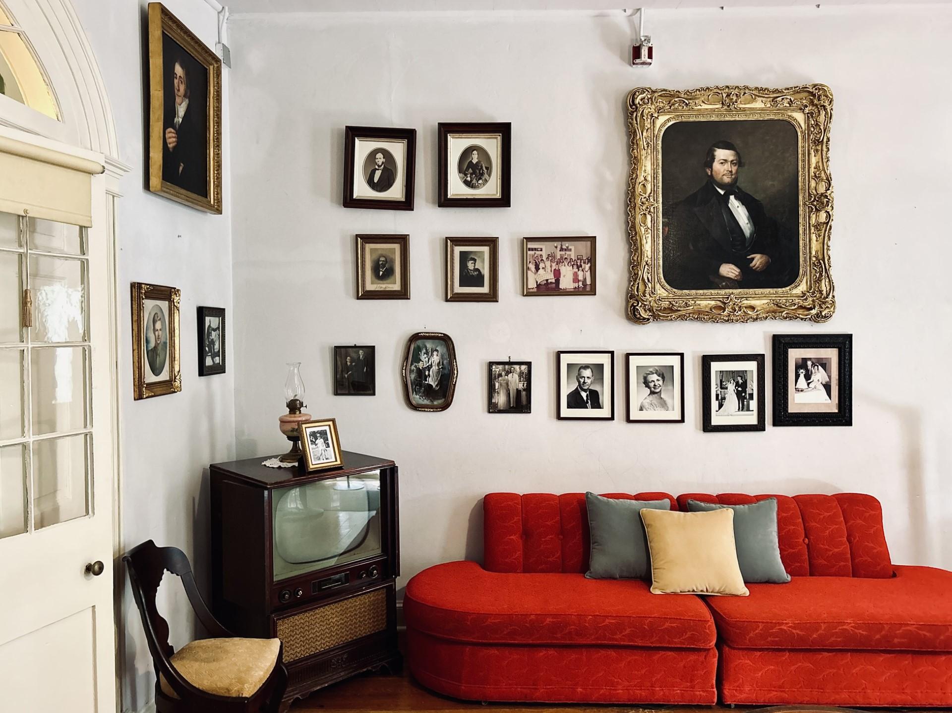The main house parlor with family portraits on the wall above a 1950s television and red sofa.