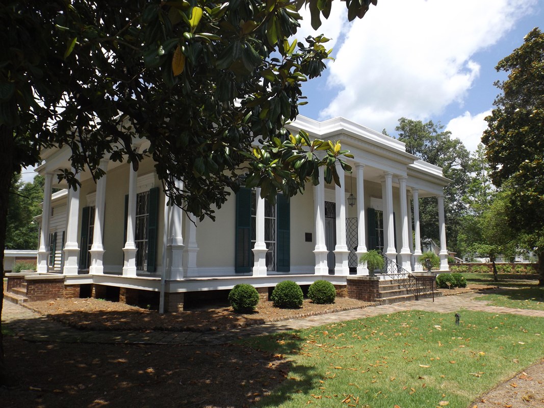 Color photo of the Verandah-Curlee House showing a white house with white columns supporting a roof.