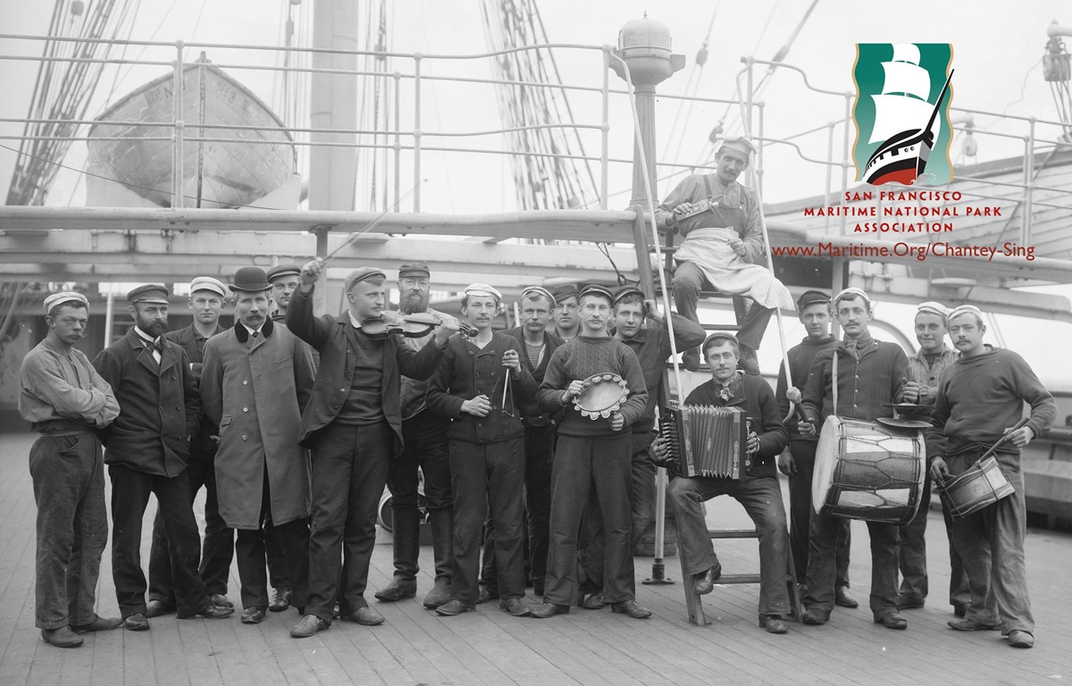 Group of men standing on the deck of a sailing ship with many holding musical instruments.