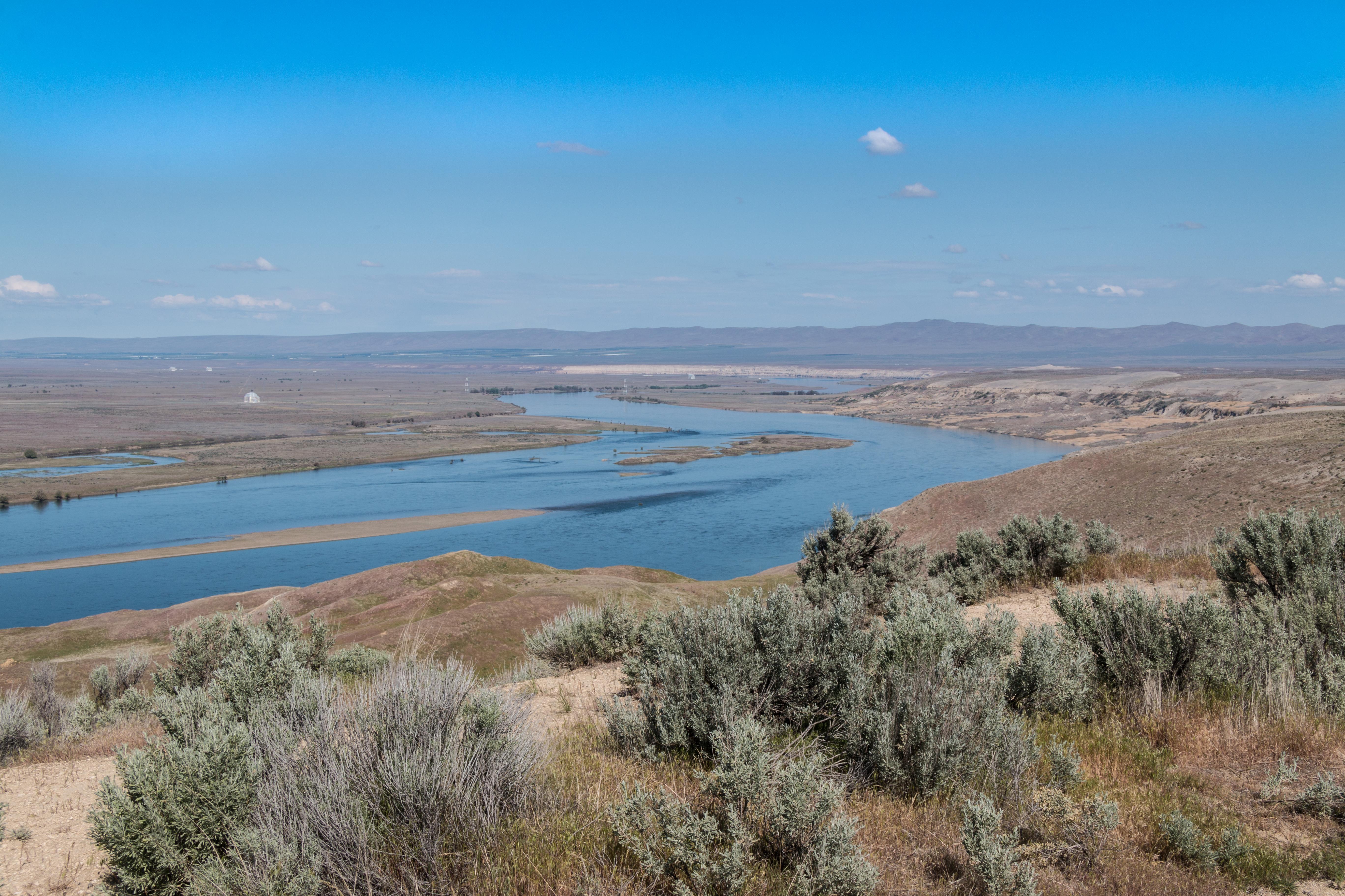 A wide river cuts through an open desert landscape on a sunny day.
