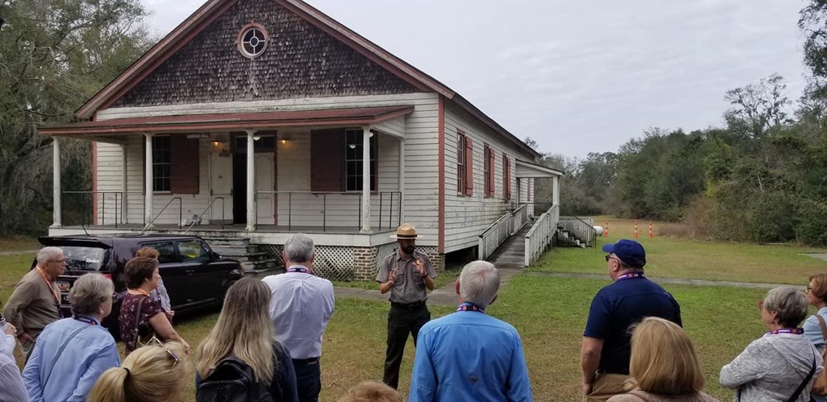 A group of people and a park ranger in front of a white wooden building