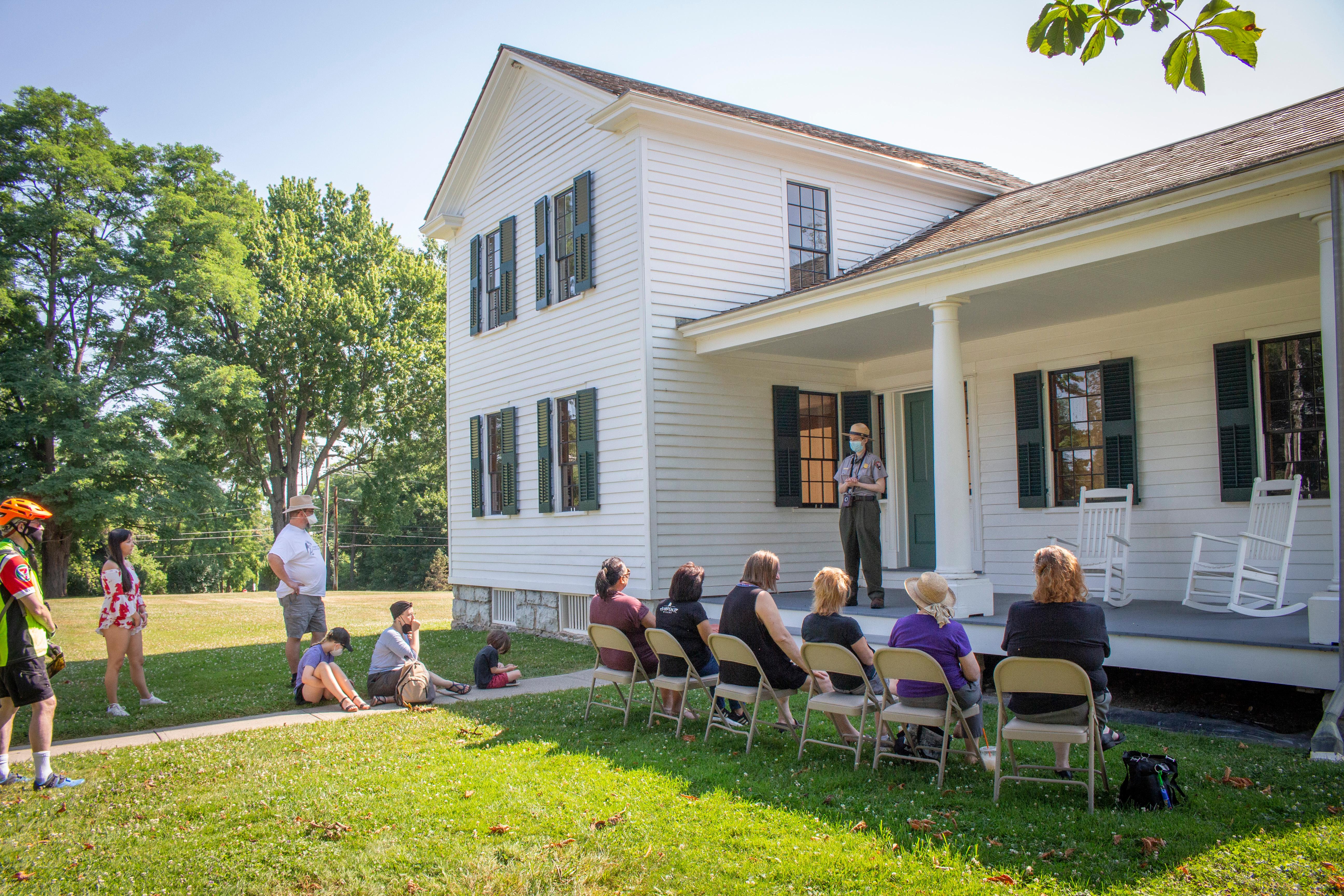 A white house with people seated in chairs in front of a large porch