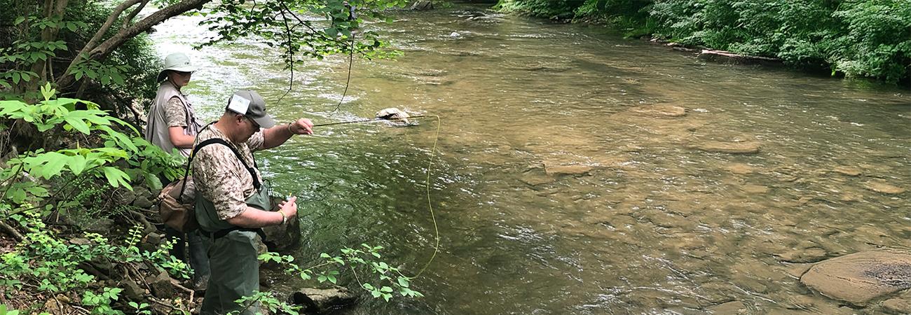 Two fishermen standing beside a rocky stream in the woods with their fishing rods