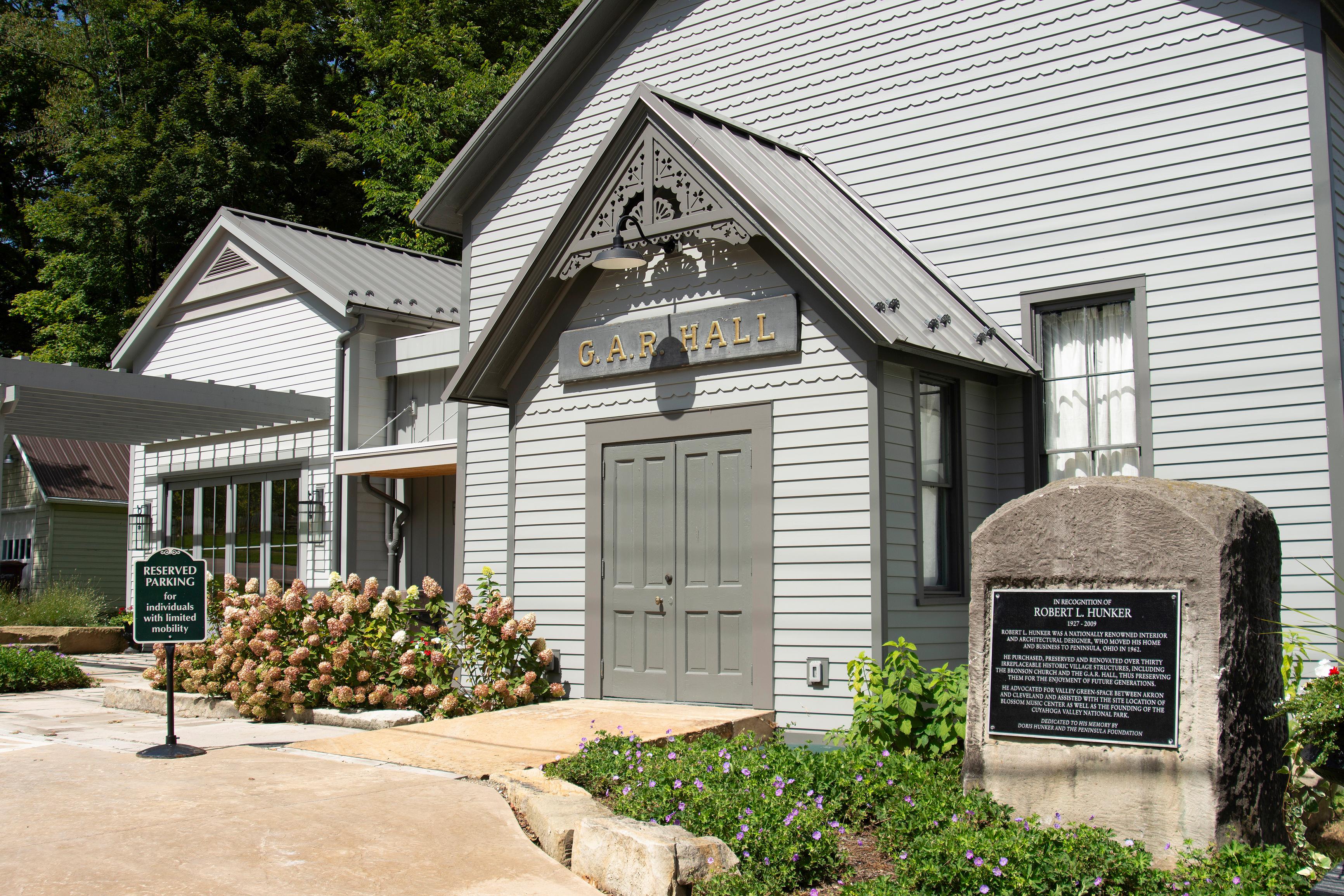 A two-story grey building with a gabled entrance. A sign above the front door reads "G.A.R. Hall".