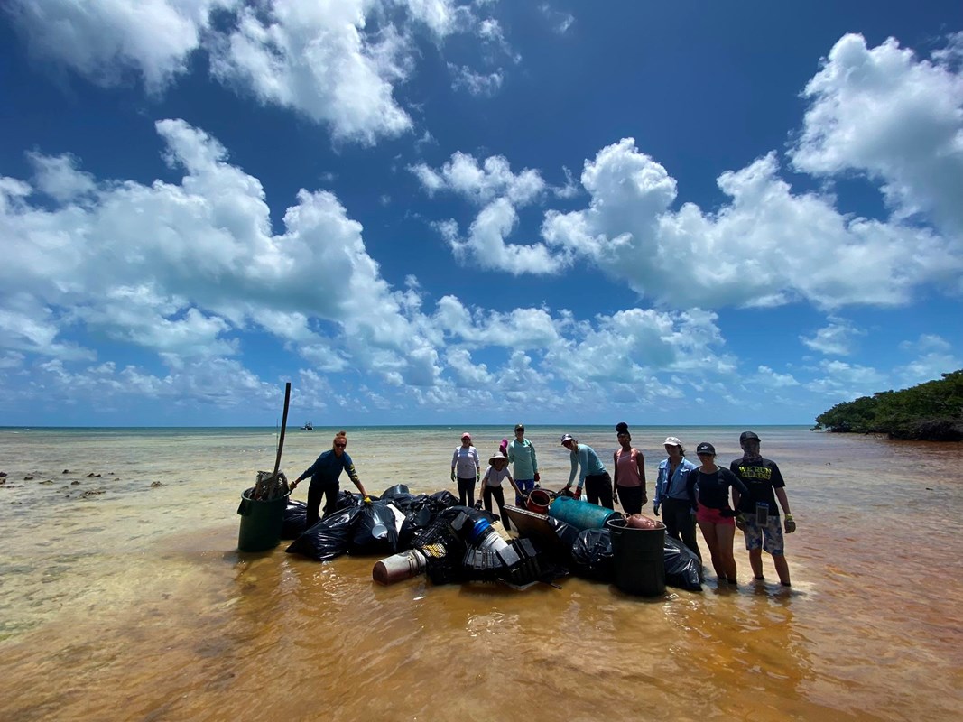 A group stands with collected trash near the ocean and a blue sky