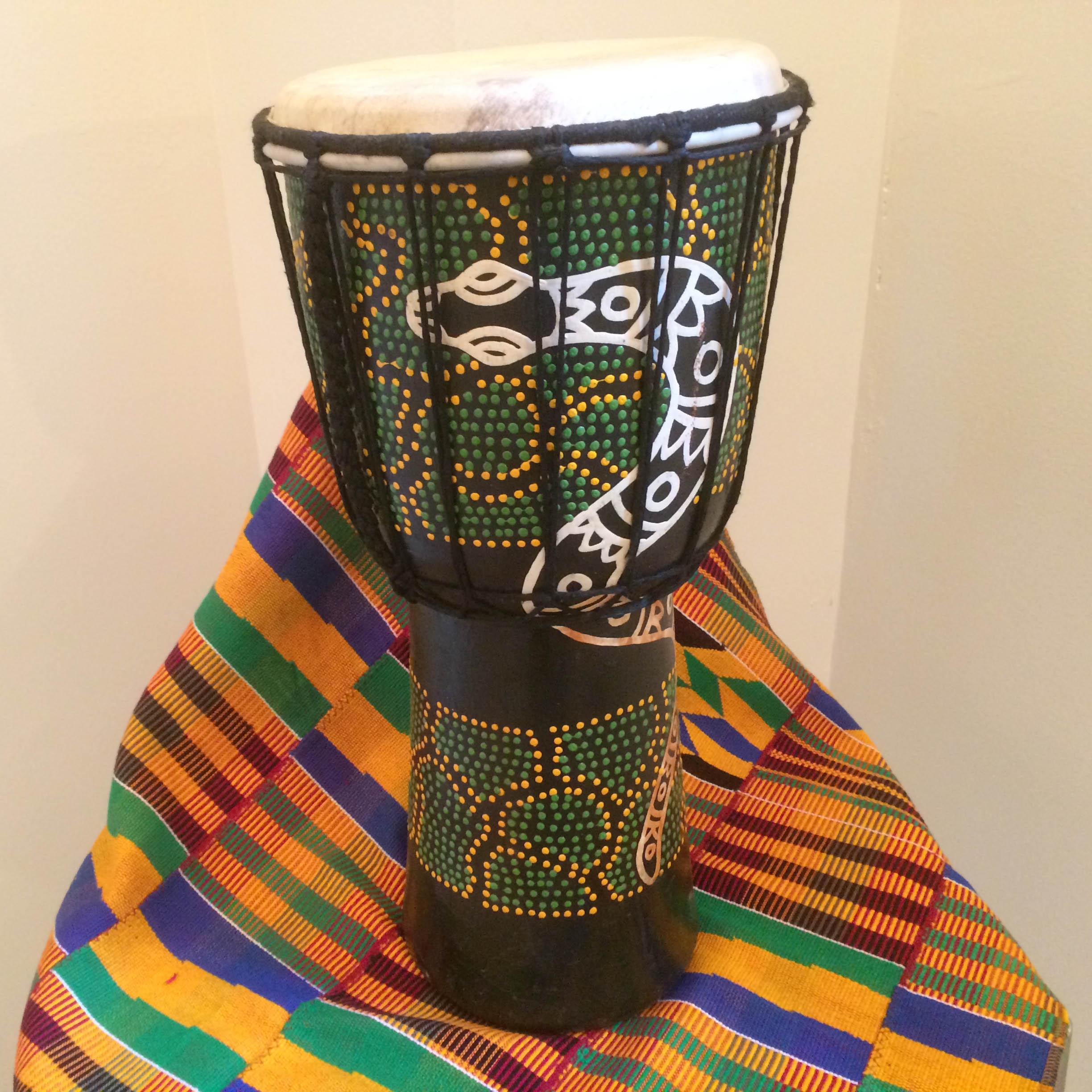 A djembe, and African drum, painted with a snake image, sits on a piece of Kente cloth.