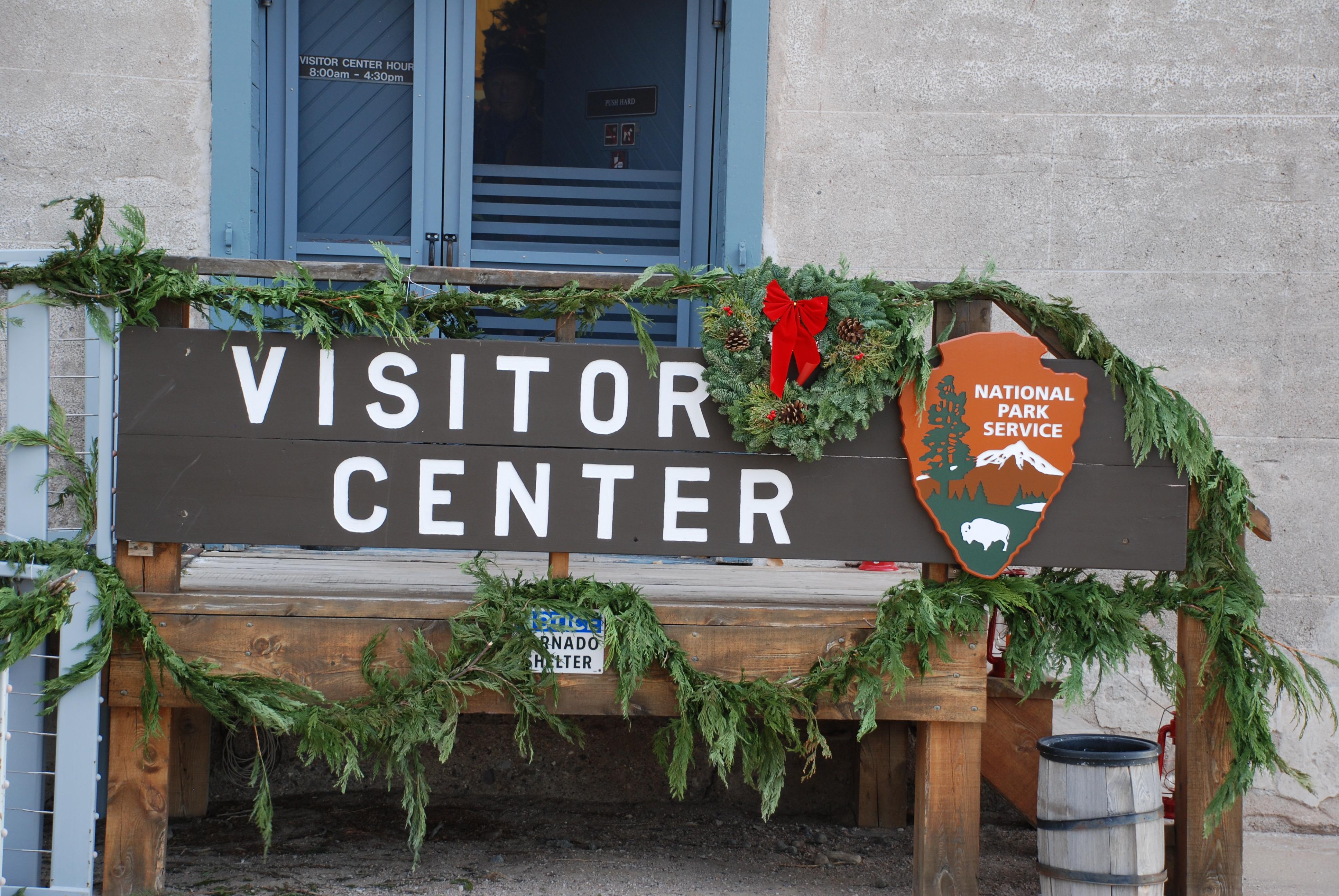A brown sign with the words visitor center on it in white lettering, with green foliage around it.